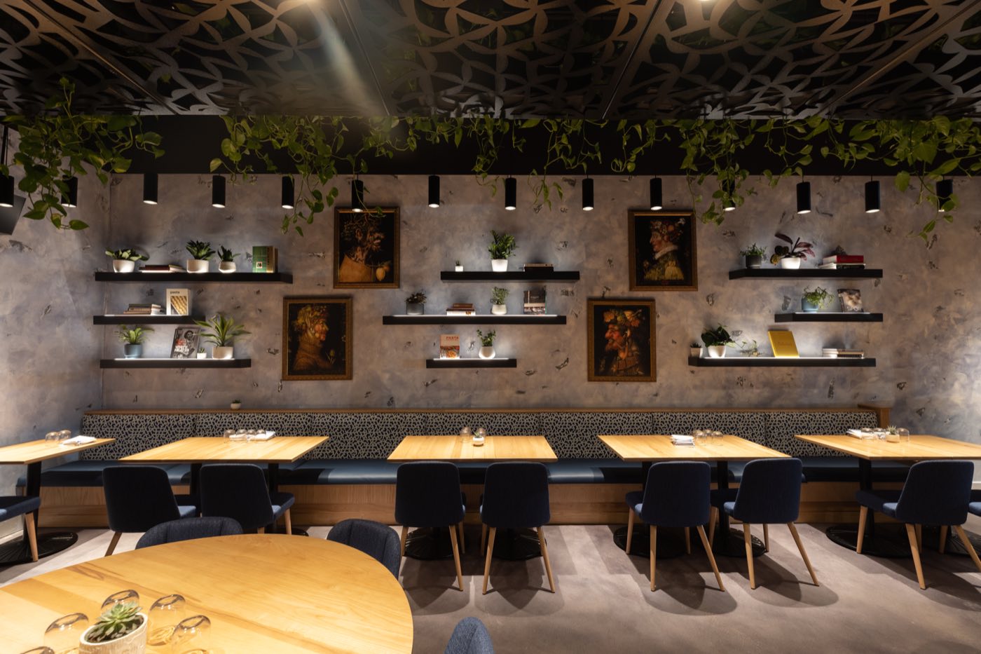 Rocca’s dining room: plaster walls, framed oil paintings, oak tables and navy chairs under a ceiling of greenery