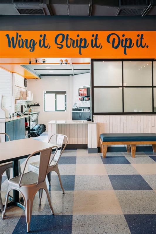 “Wing it, Strip it, Dip it” sign above the kitchen pass